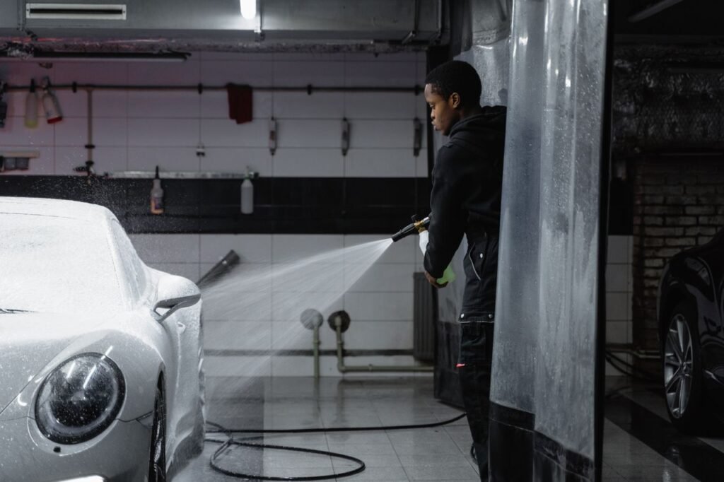 A person using a pressure washer to clean a car in an indoor garage setting.
